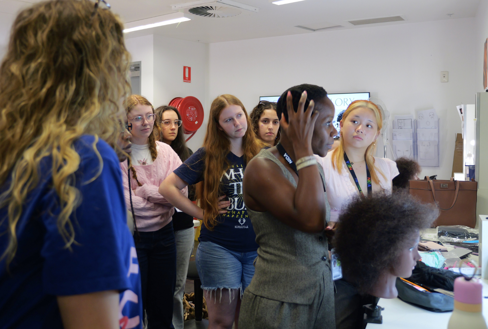 Students in a classroom stand behind a lecturer who is demonstrating how to look after curly hair.