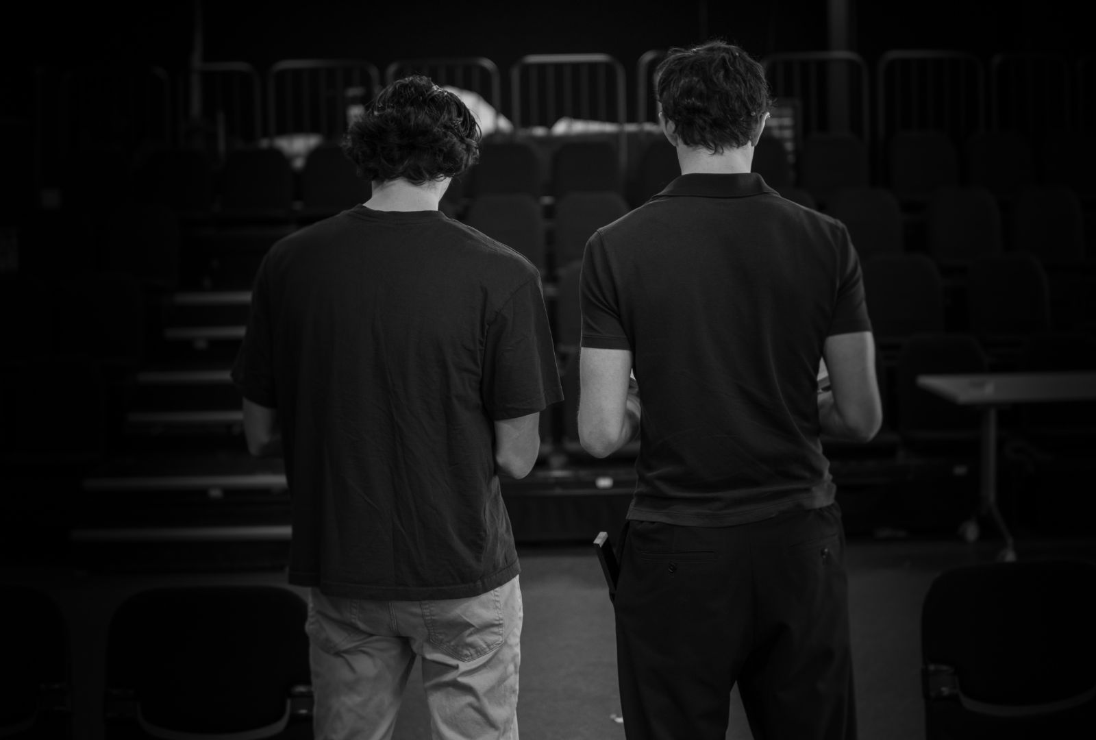 Two men stand in a theatre with their backs to the camera.