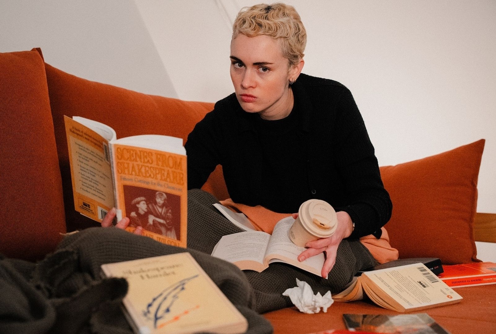 A woman in a room holding a coffee and a book surrounded by rubbish.