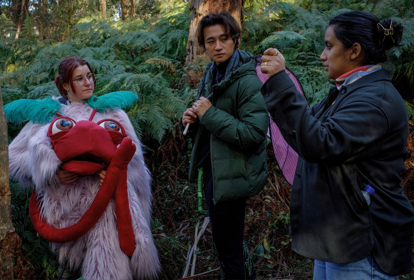 A director directing an actor and a person wearing a costume in the woods.
