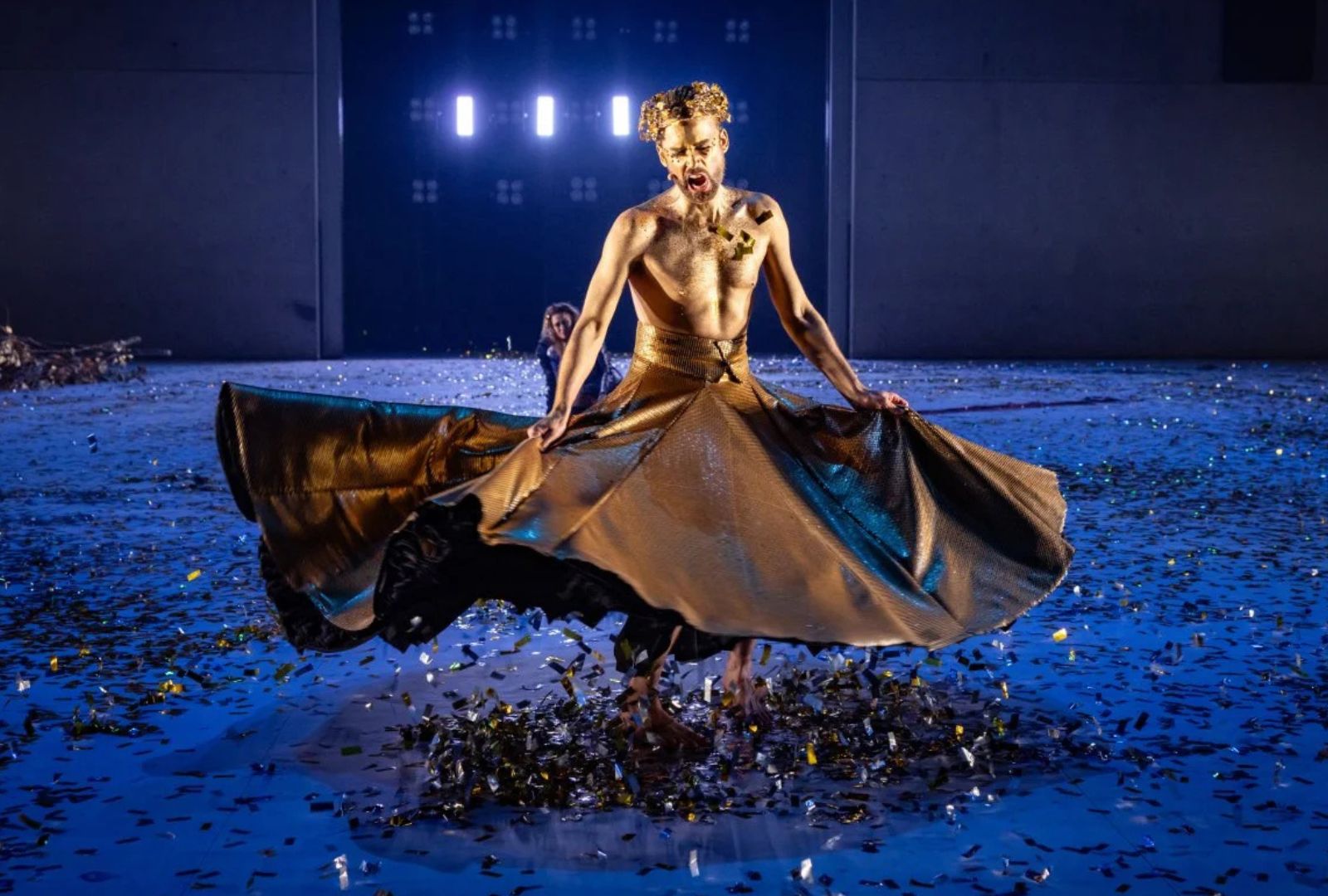 A man in golden cloth painted gold with blue lighting.