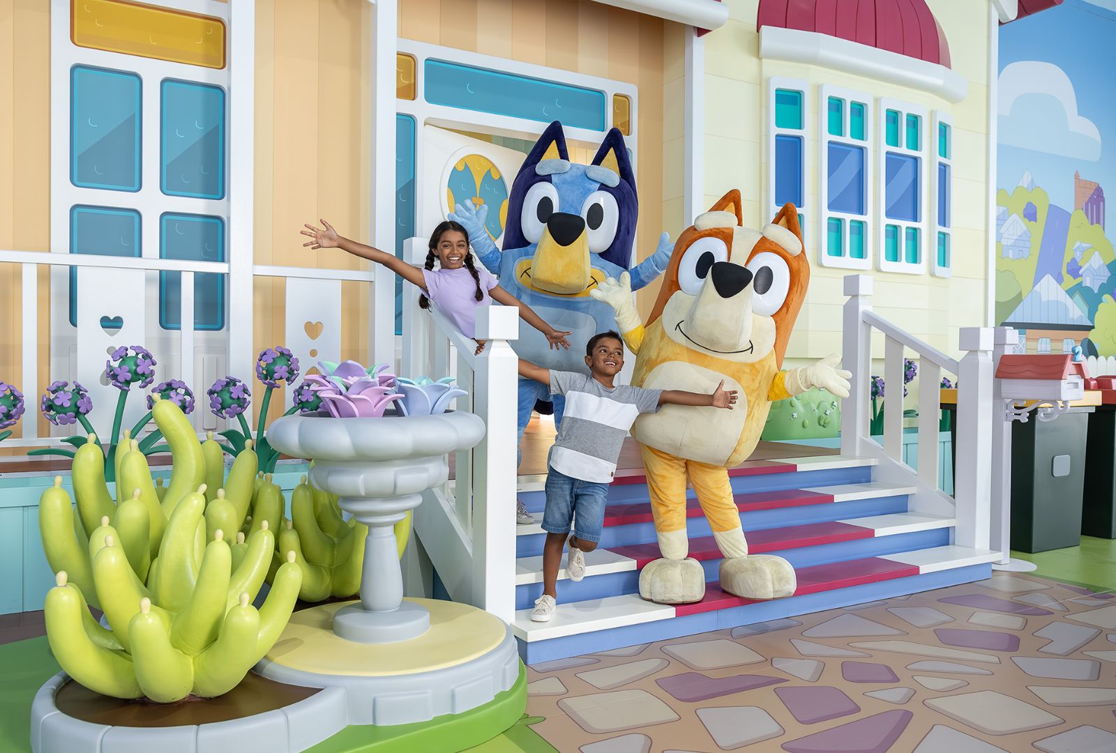 Two children outside a fake house with two mascots from the children's series 'Bluey'.