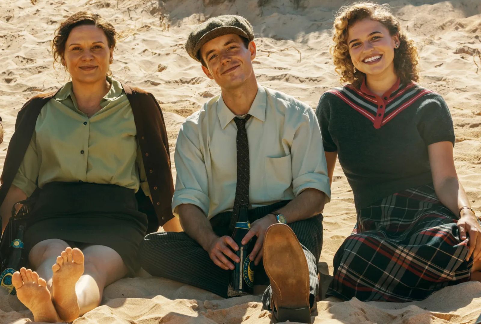 Three people sitting on a beach smiling.