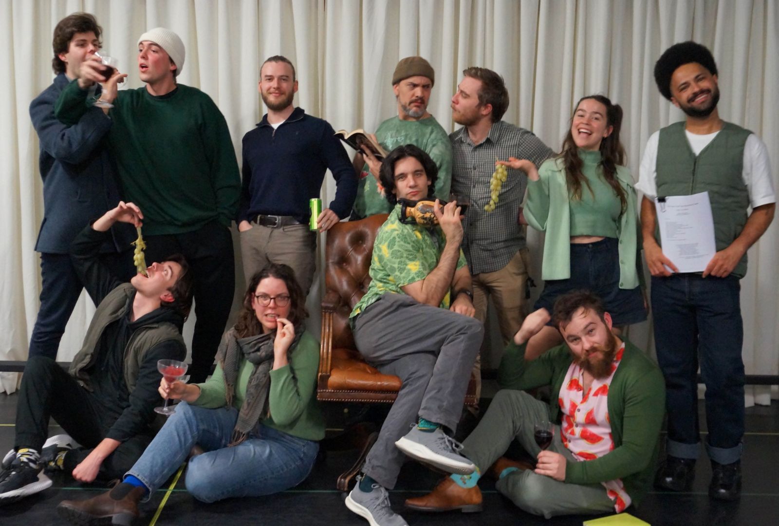 A group of people posing for a photo holding grapes and wine glasses, being silly.