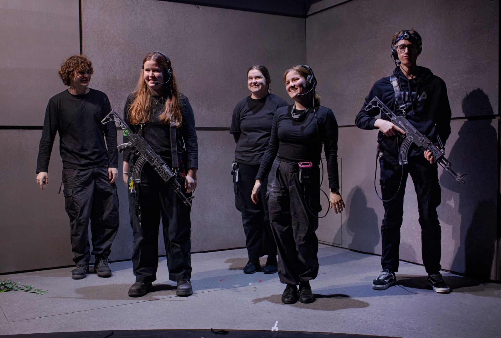 Five people on a stage wearing all black, two holding fake guns.