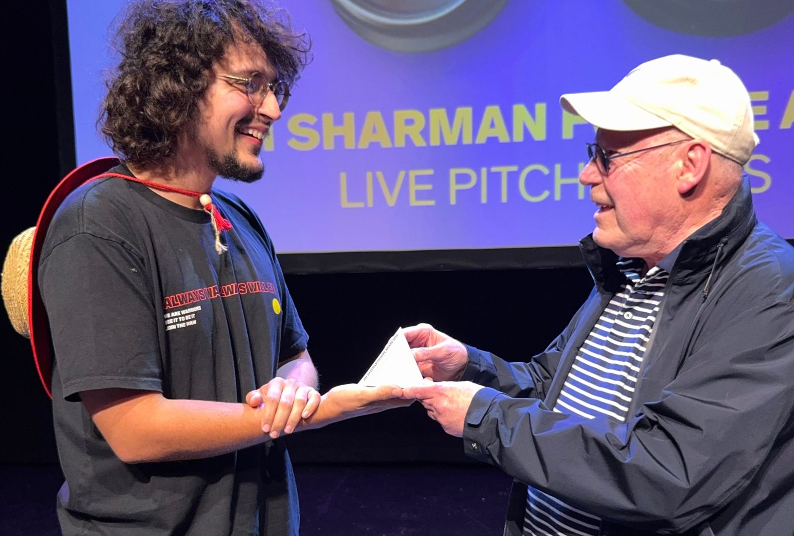 Daniel MacKenzie (left) receiving the Jim Sharman Future Award from Jim Sharman (right). He holds a pyramid-shaped trophy.