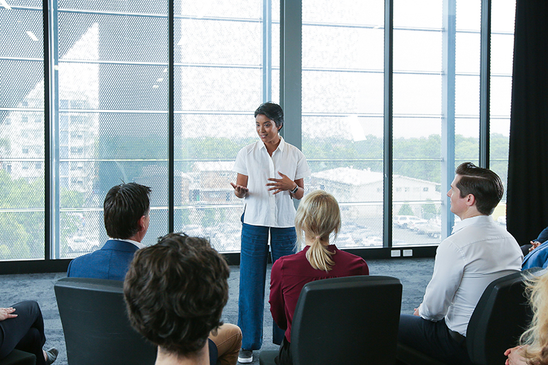 A woman speaking to a crowd of seated people, in a professional context