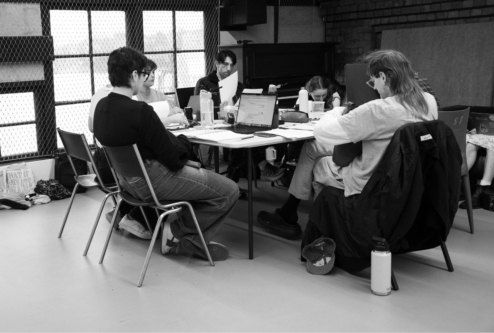 Five people sit at a table doing a reading of a play.