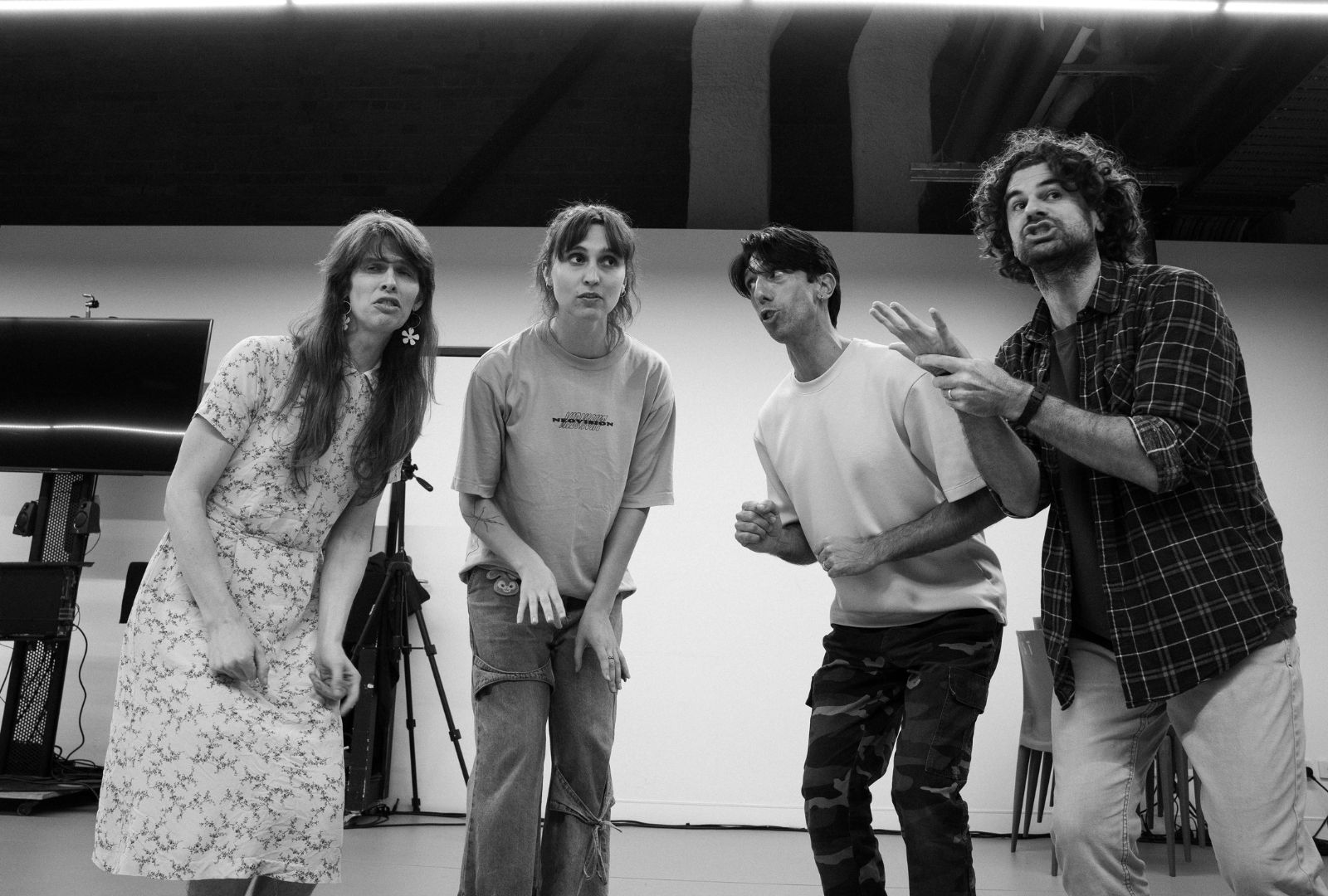 Four people in a rehearsal room singing and leaning forward towards the camera.