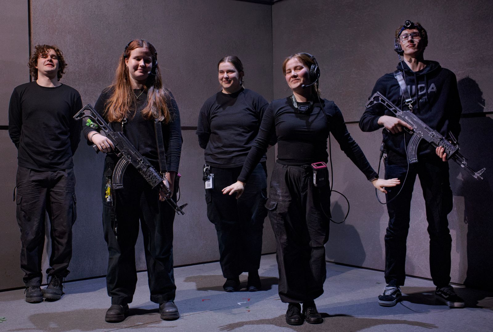 Five people on a stage wearing all black, two holding fake guns.