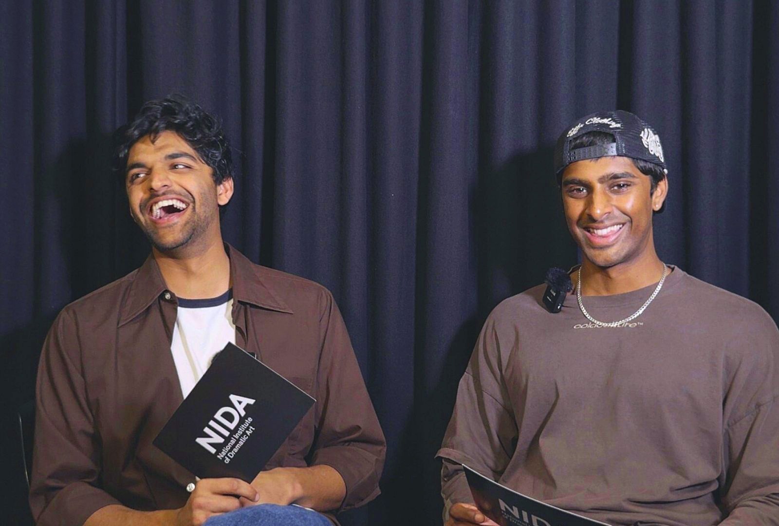 Two men in front of a curtain smiling.