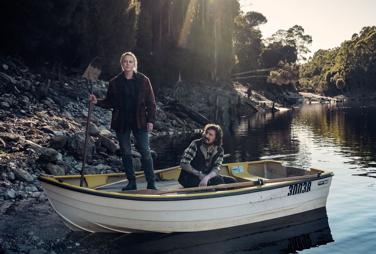 Two people standing on a boat pulled into a bank.