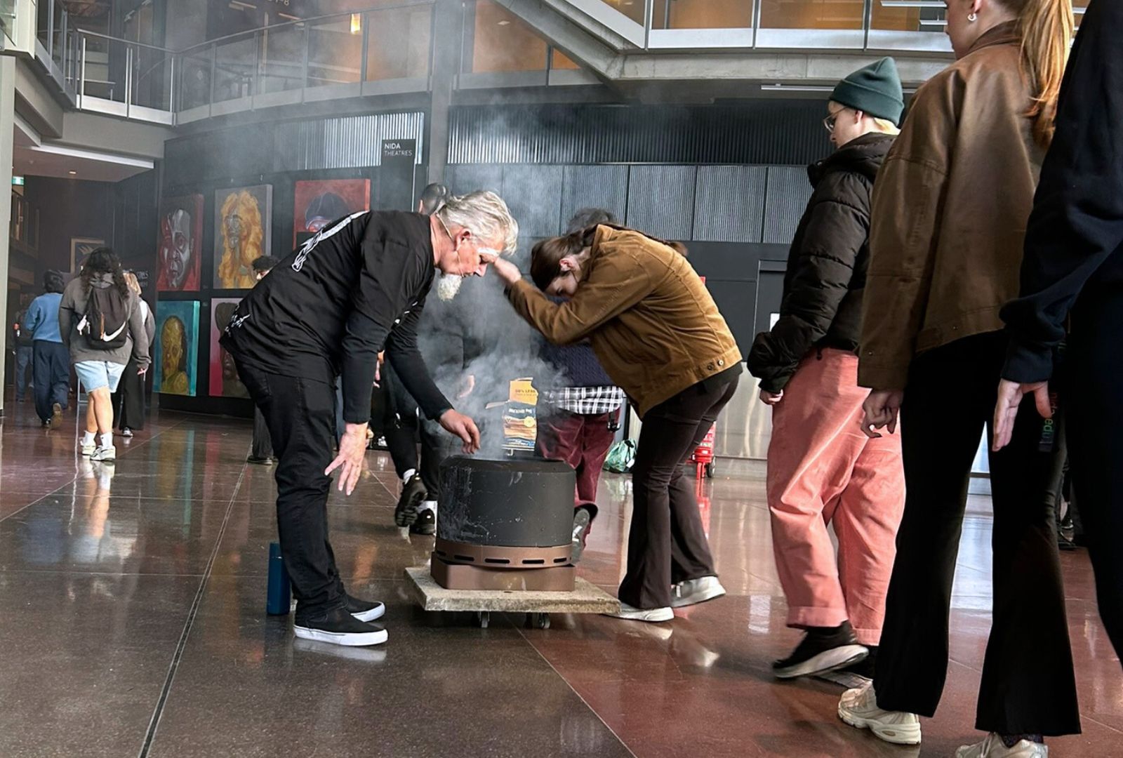 Uncle Matthew Doyle is leaned over a fire pit, performing a smoking ceremony with a line of people participating.